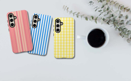 Colorful striped and checkered phone cases for iPhone 14 Pro Max and Samsung S22 alongside a cup of coffee on a white table