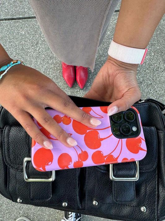 Person holding phone with cherry-themed case over a black handbag