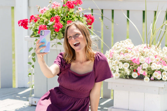 Woman taking a selfie outdoors with a stylish and durable phone case in front of a floral background