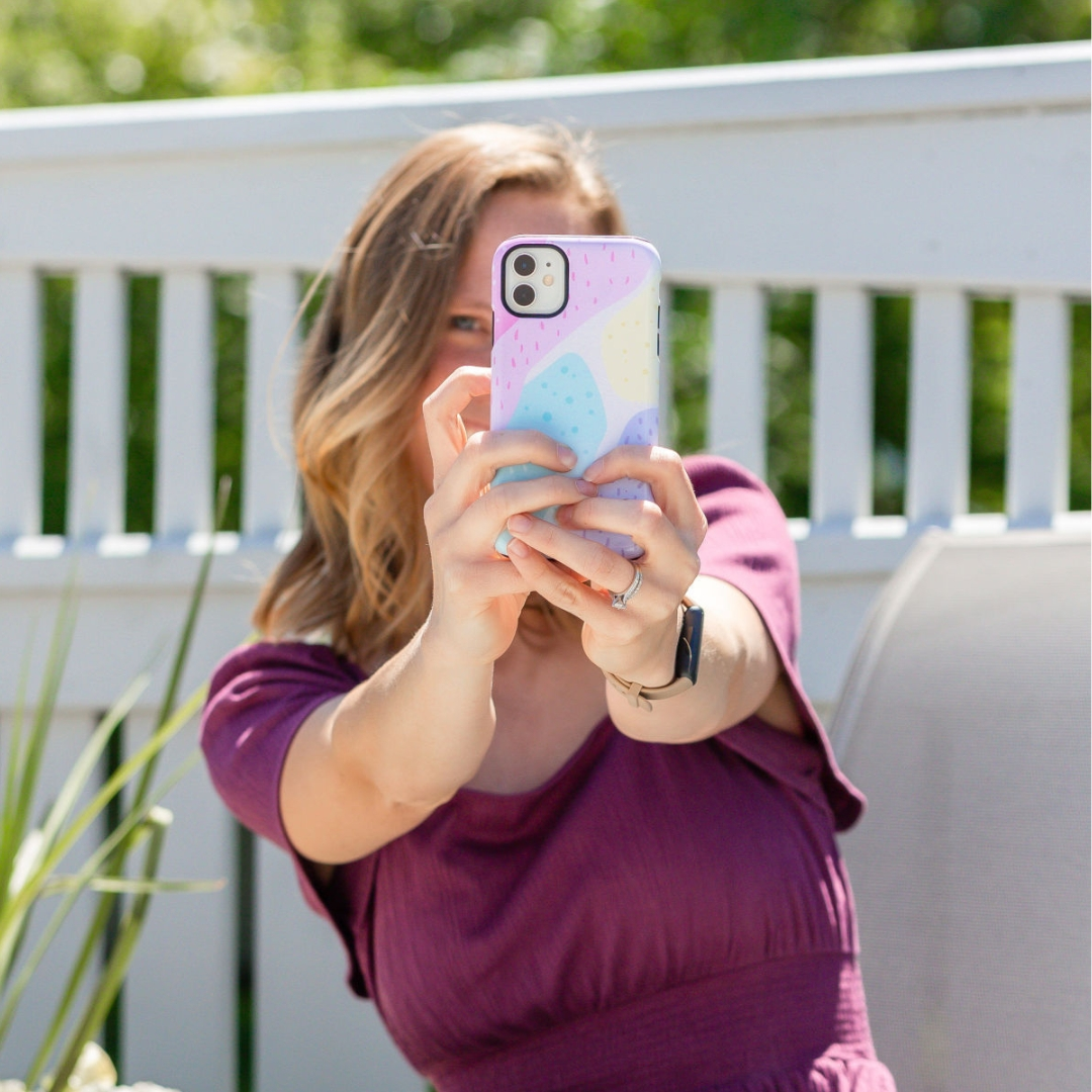 Woman taking a selfie with an aesthetic, cute iPhone case on an iPhone 11 in a bright outdoor setting.